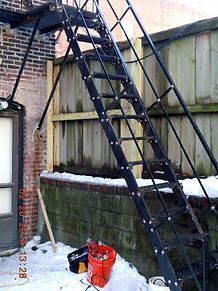 A fire escape is sitting in the snow next to a brick building.