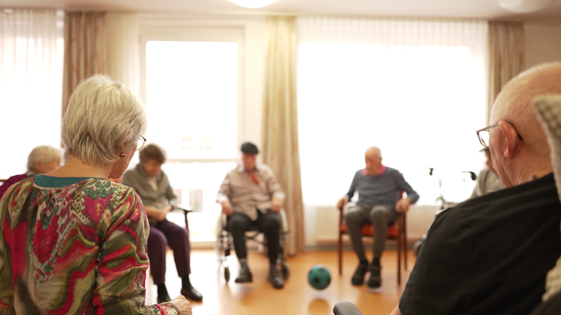 Eine Senior*innengruppe sitzt im Kreis und werfen sich einen Ball zu