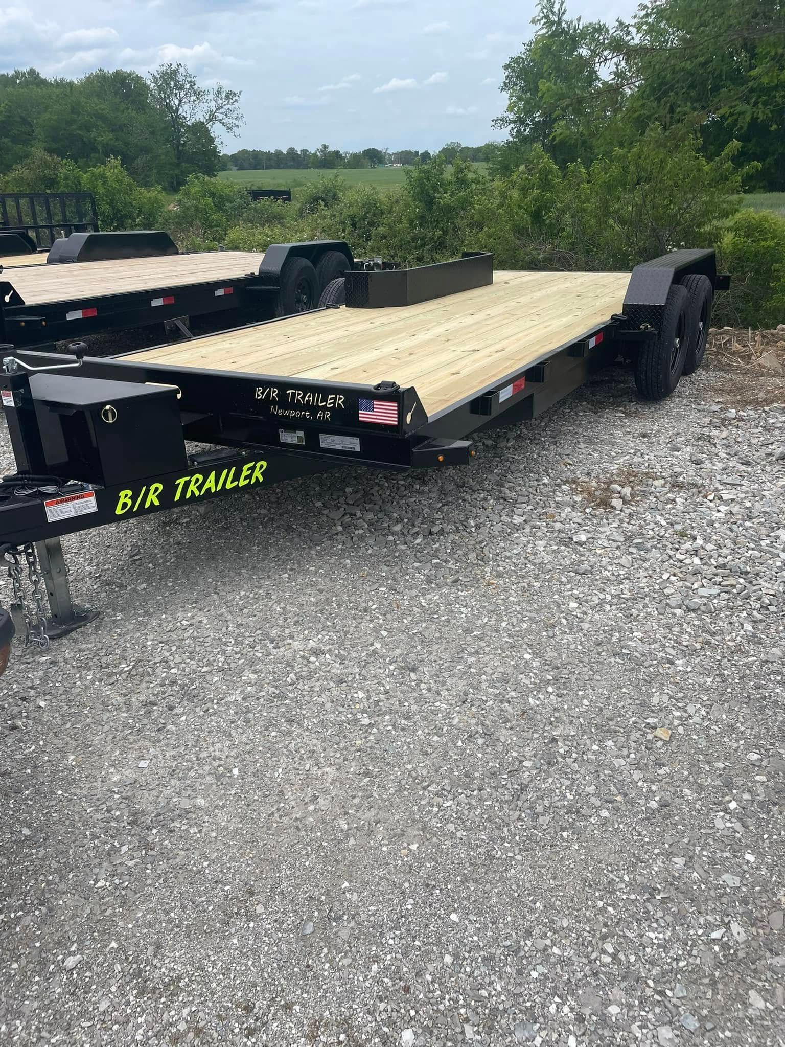A flatbed trailer is sitting on top of a gravel road.