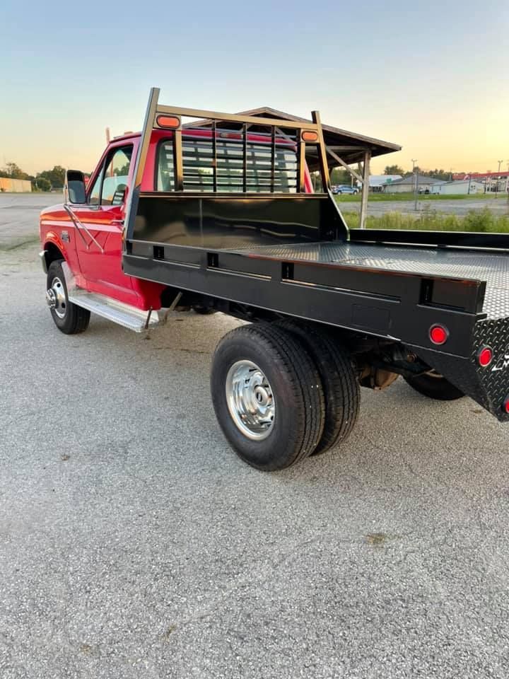 A red truck with a flat bed is parked on the side of the road.