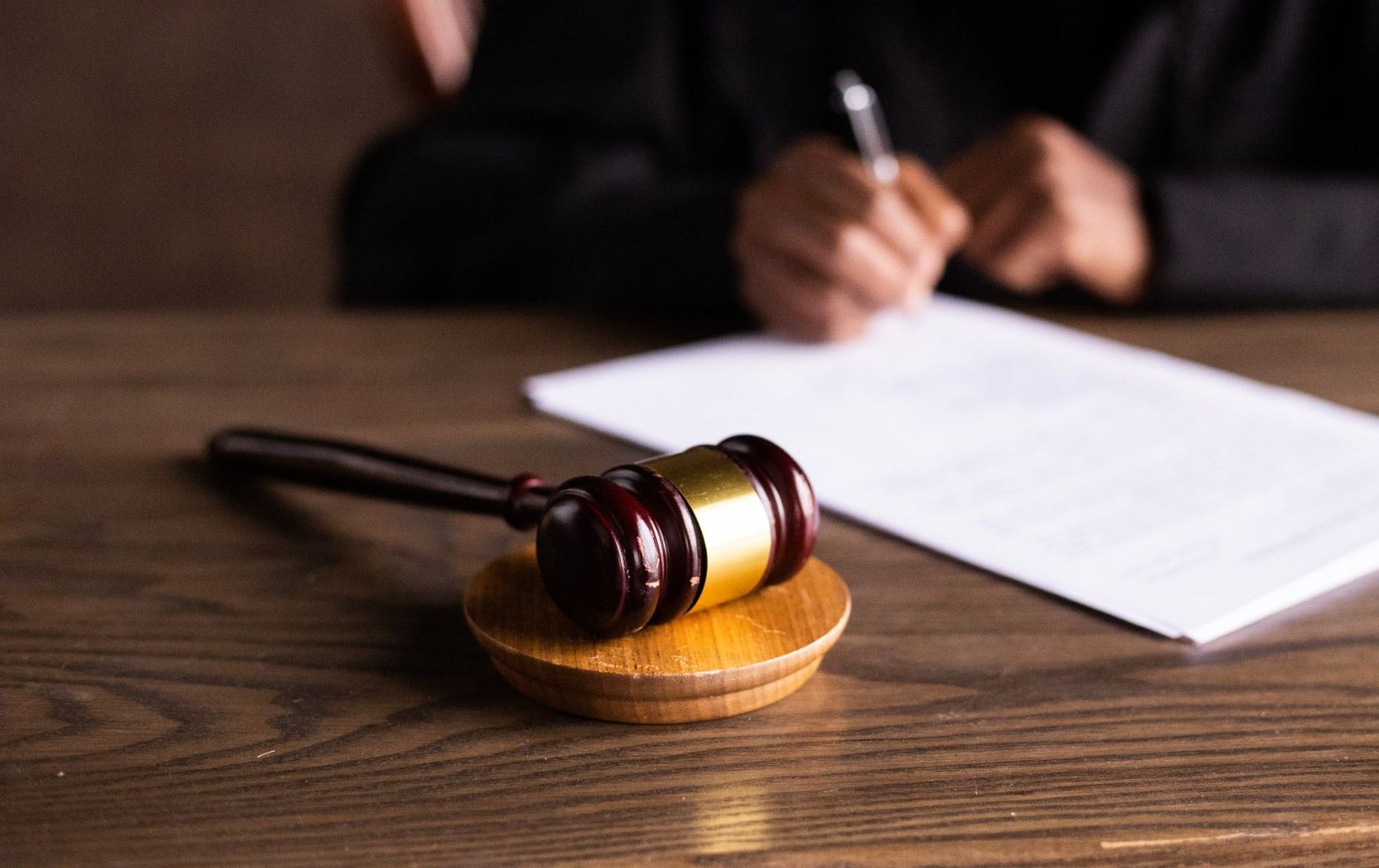 Judge’s gavel on a wooden desk with a person writing in the blurred background