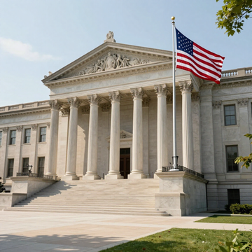 A historic, neoclassical government building with tall stone columns and a large staircase, featuring a waving US flag.