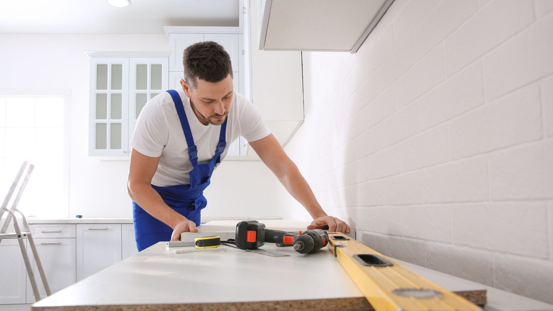 A man is working on a kitchen counter with a drill and a level.