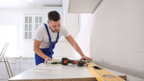 A man is working on a kitchen counter with a drill and a level.