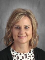 A woman wearing a leopard print shirt and a black jacket is smiling for the camera.