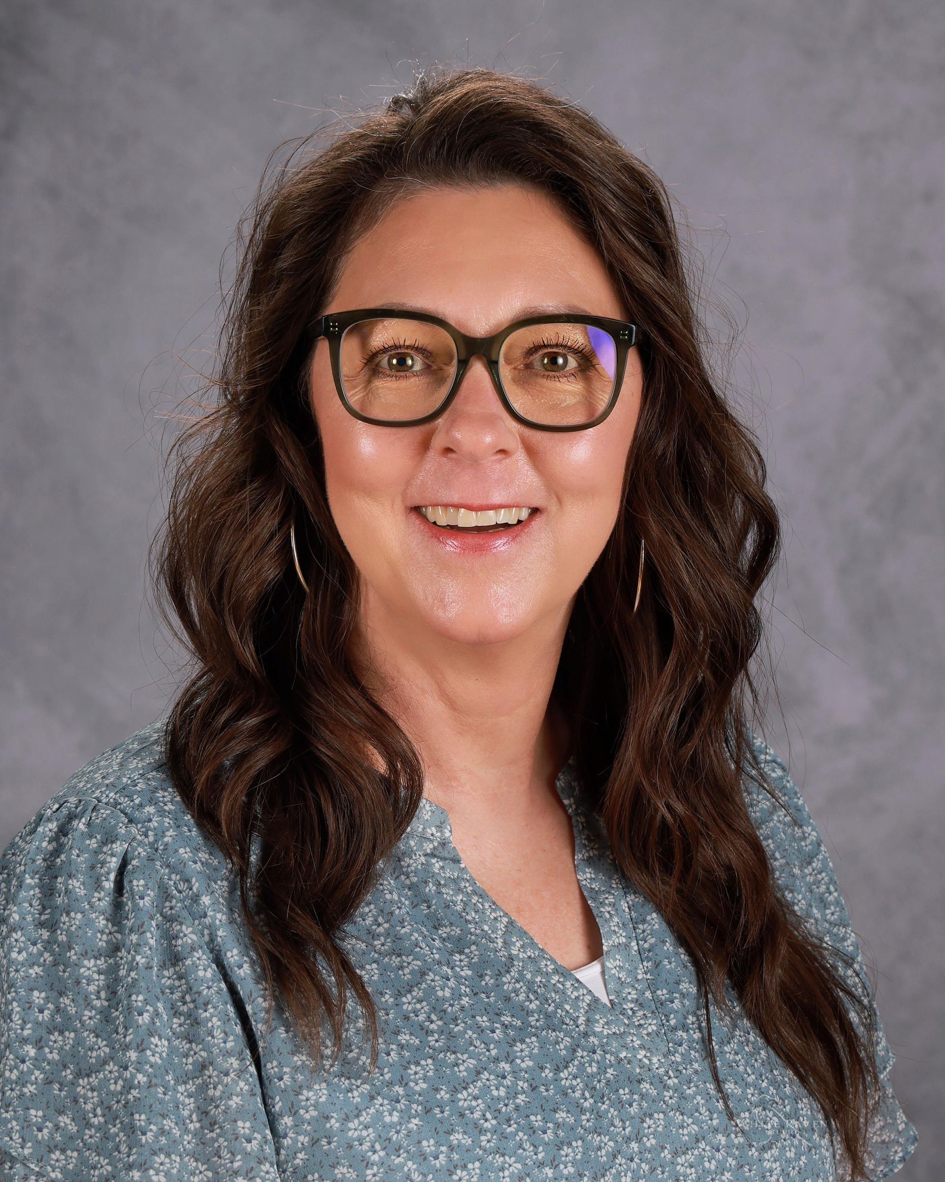 A woman wearing glasses and a yellow shirt is smiling for the camera.