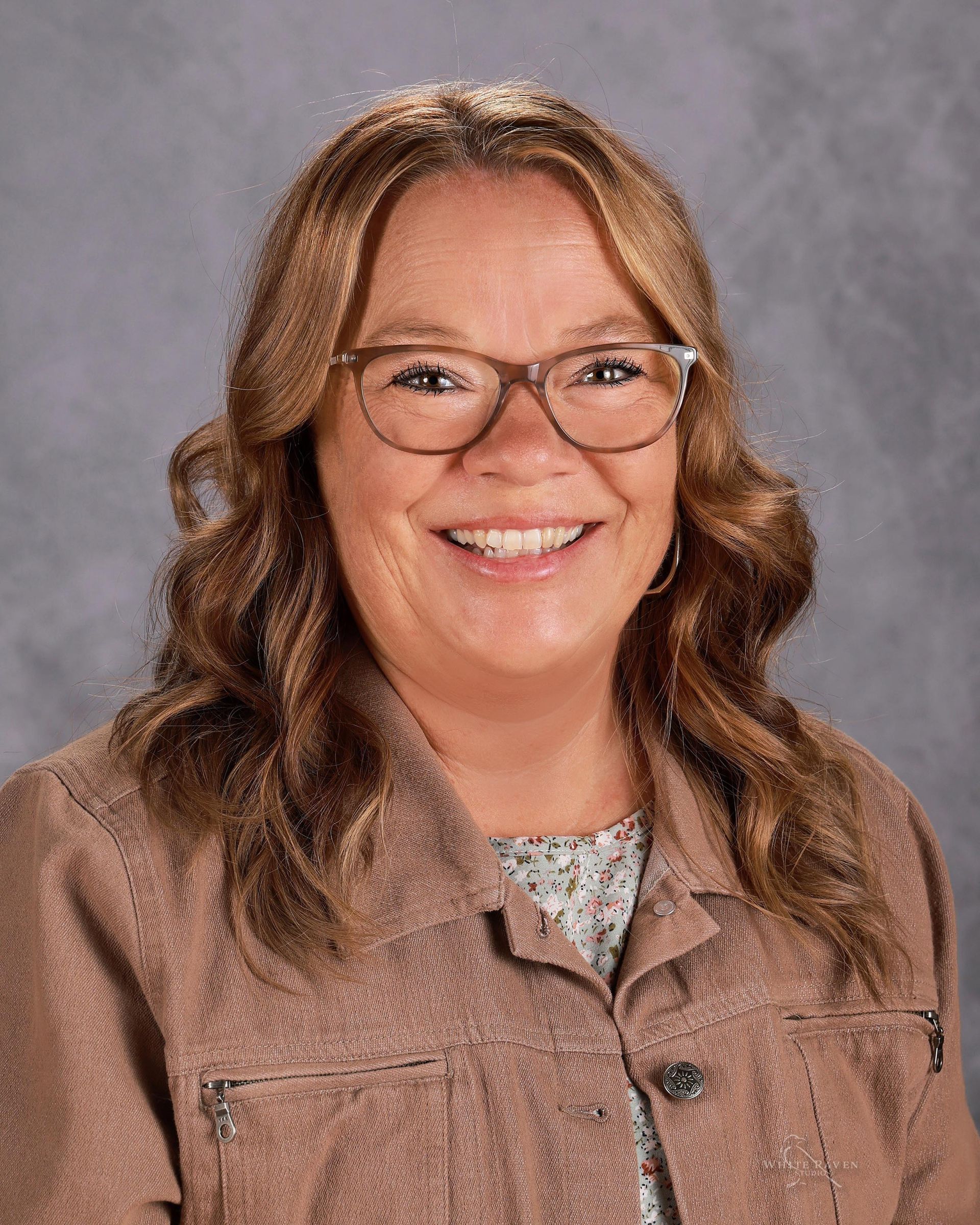 A woman wearing glasses and a blue shirt is smiling for the camera.