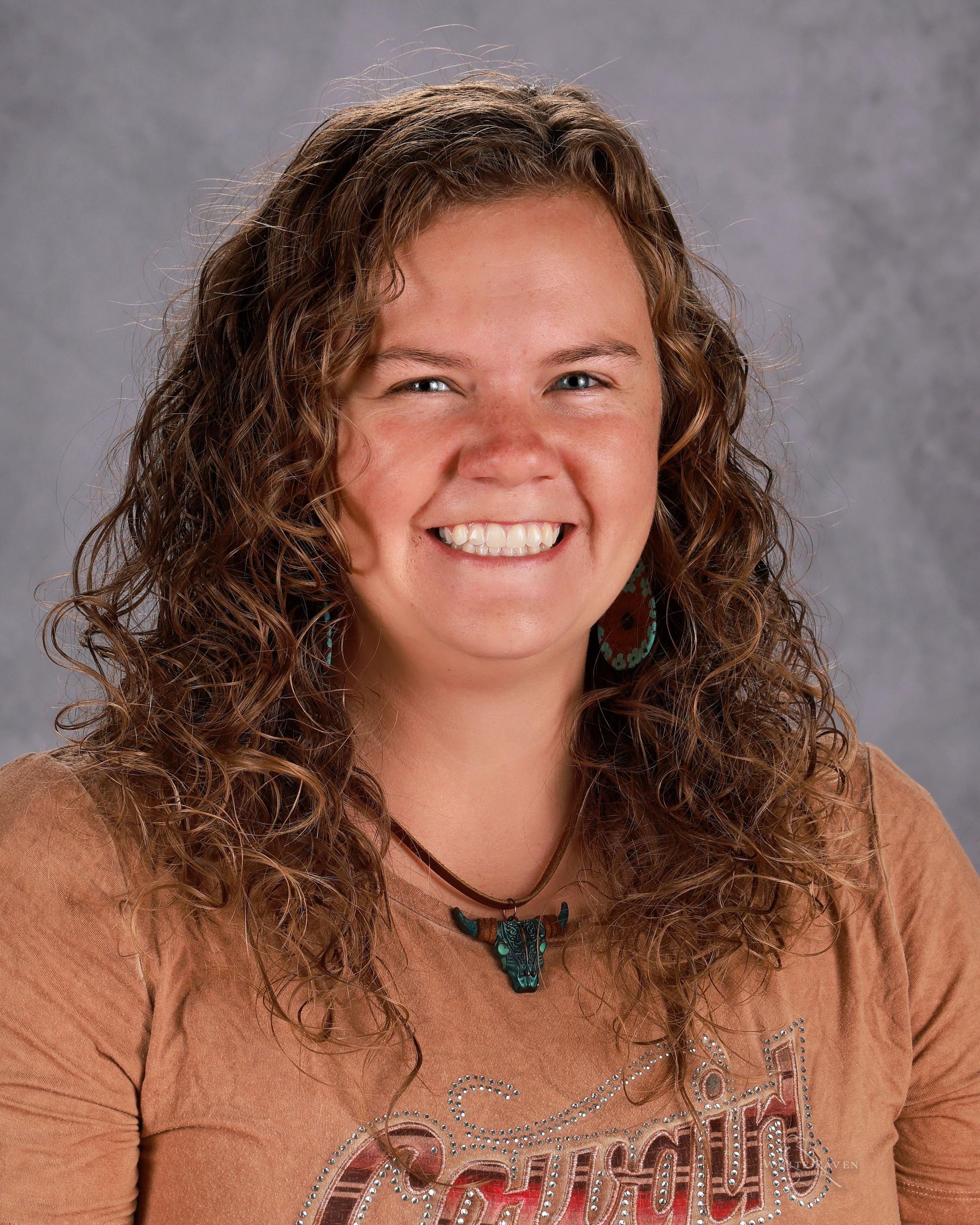 A woman with curly hair is smiling and wearing a necklace.