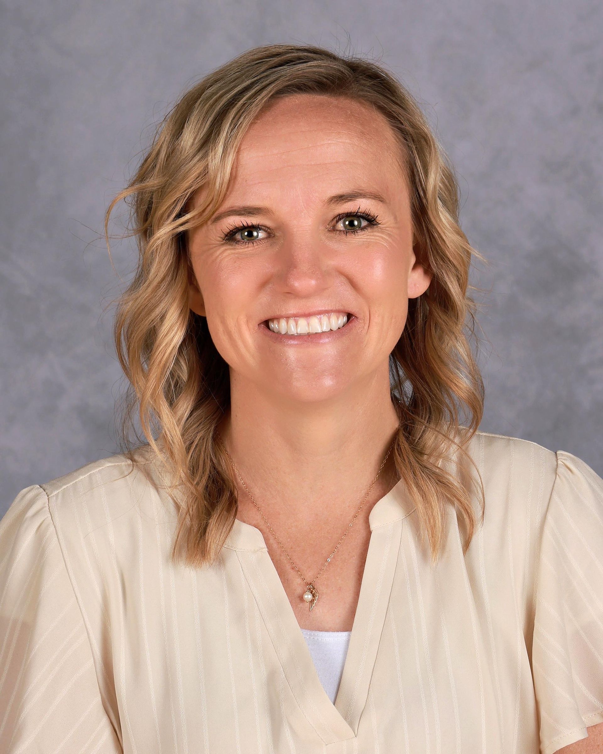 A woman wearing a white shirt and a necklace is smiling for the camera.