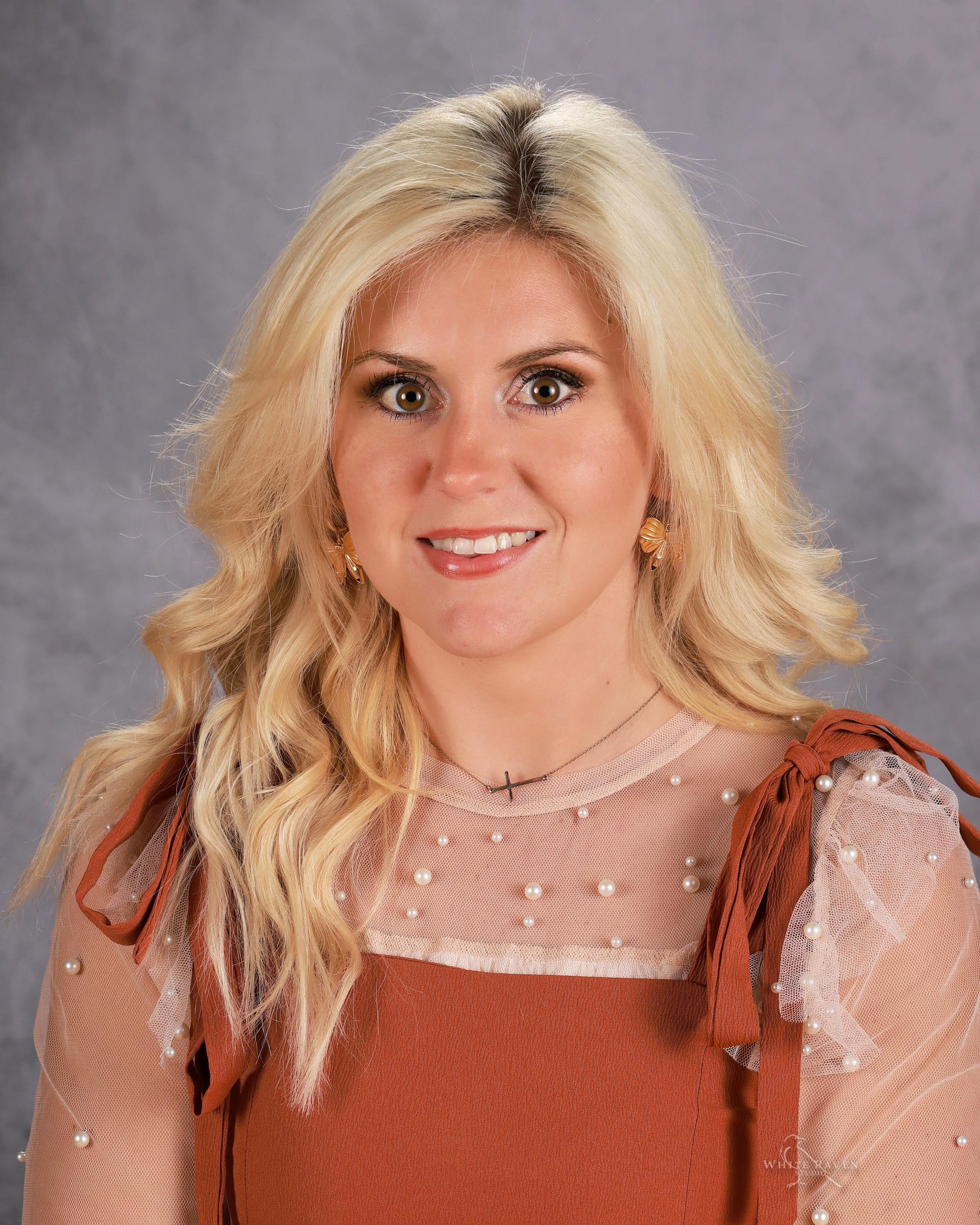 A woman with blonde hair and a necklace is smiling for the camera.