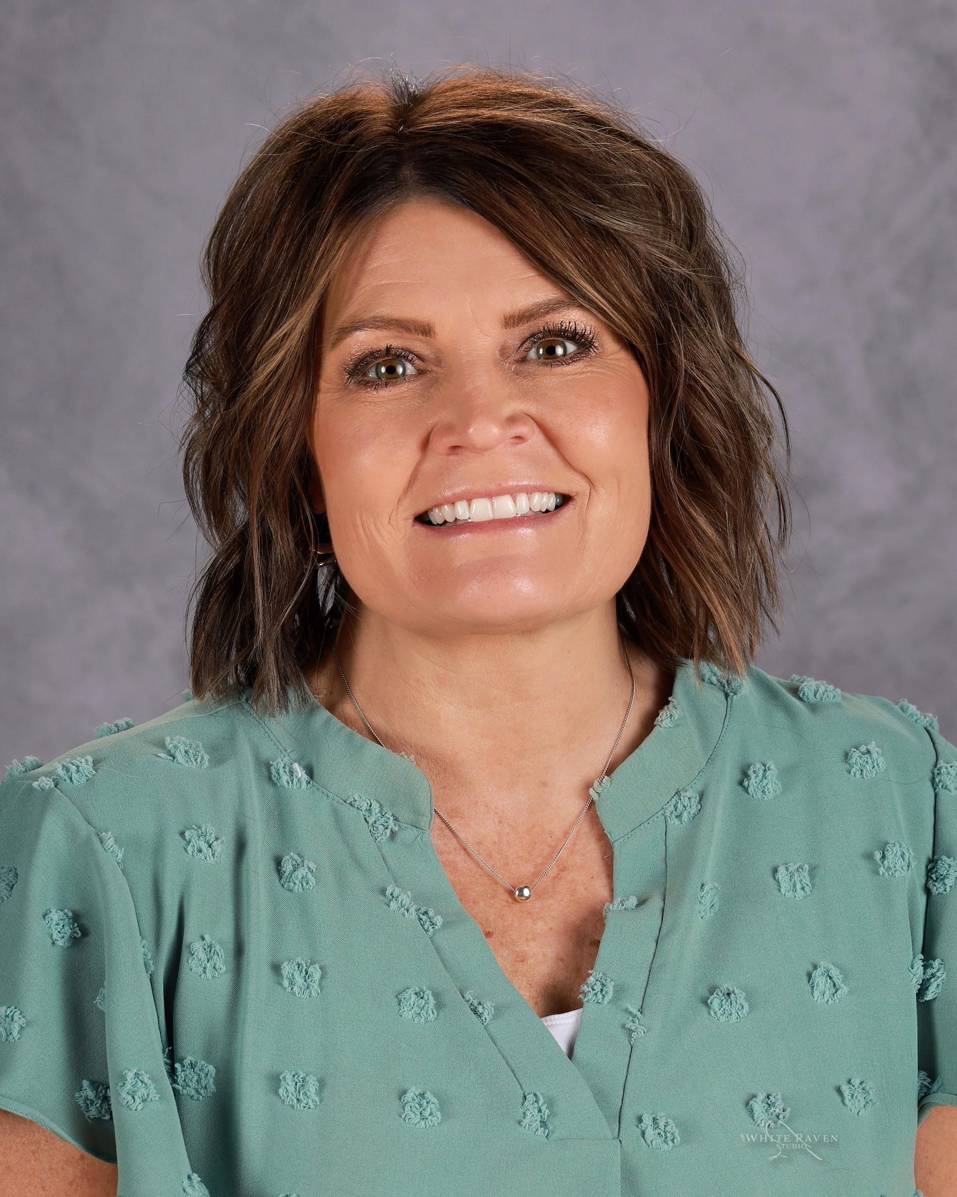 A woman wearing a brown shirt and a necklace is smiling for the camera.
