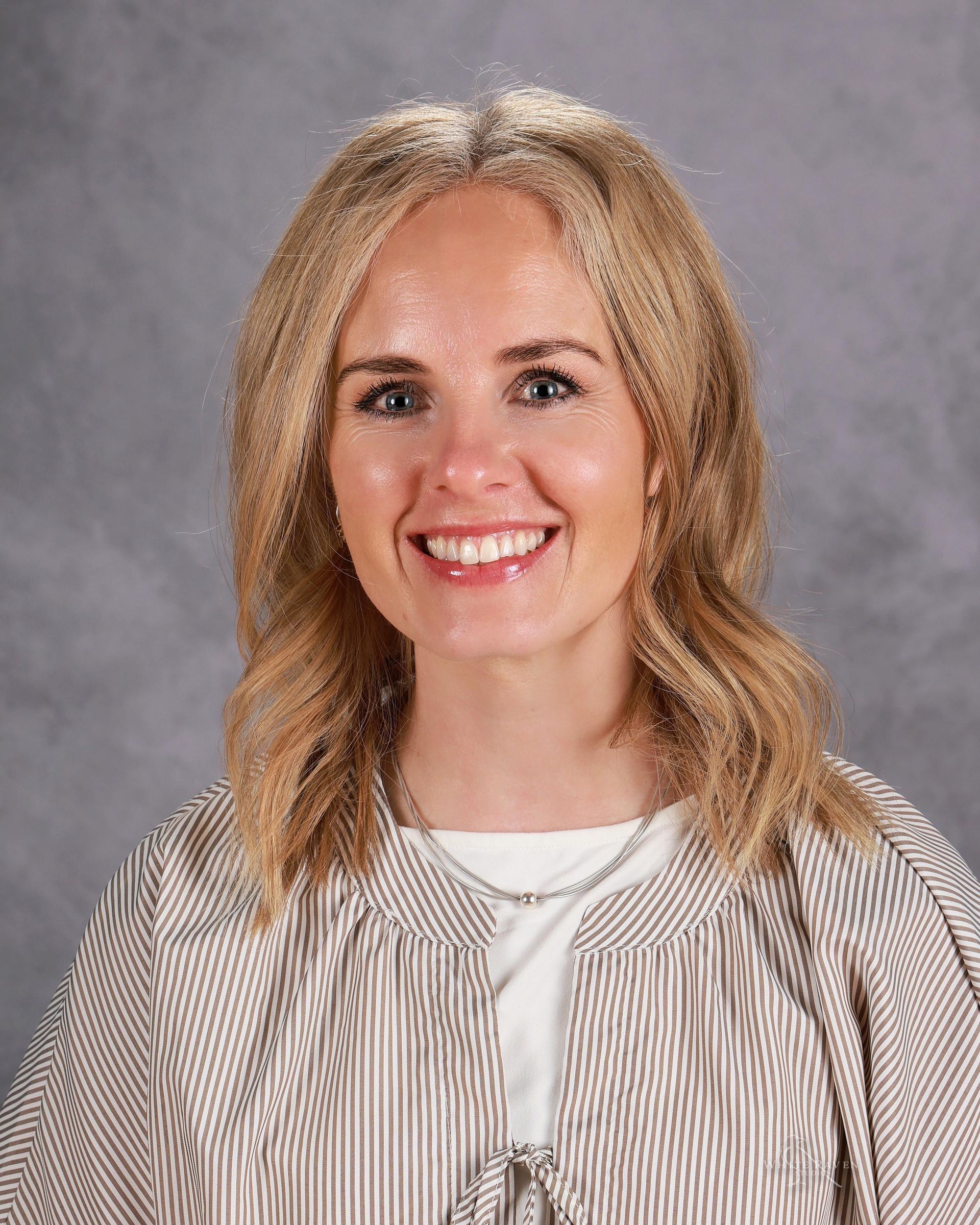 A woman with blonde hair and a necklace is smiling for the camera.