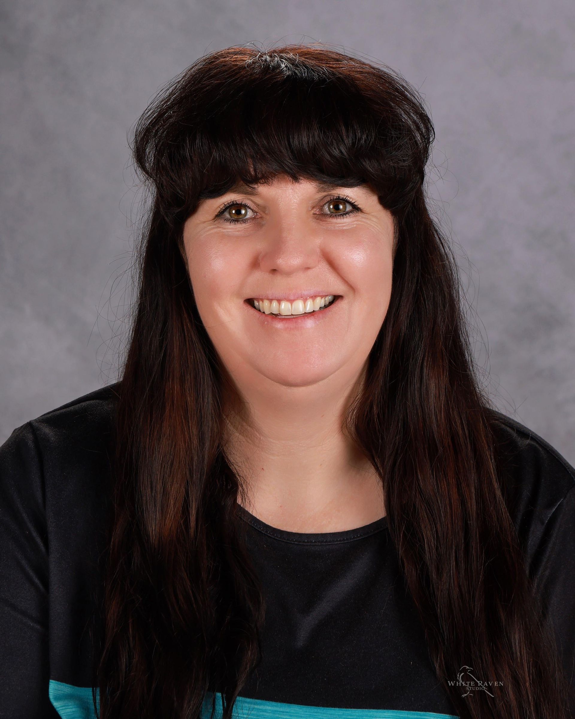 A woman with long brown hair and bangs is smiling for the camera.