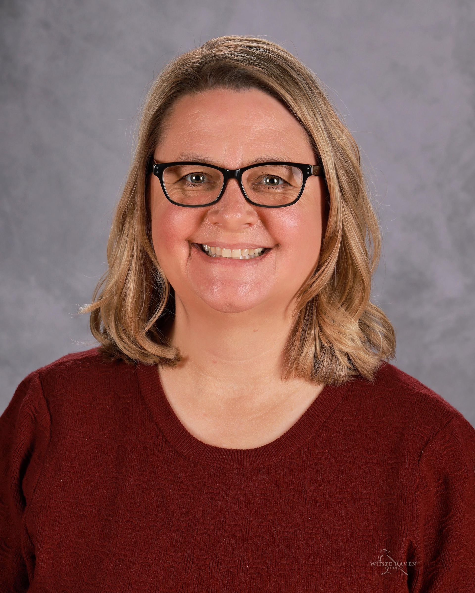 A woman wearing glasses and a blue shirt is smiling for the camera.