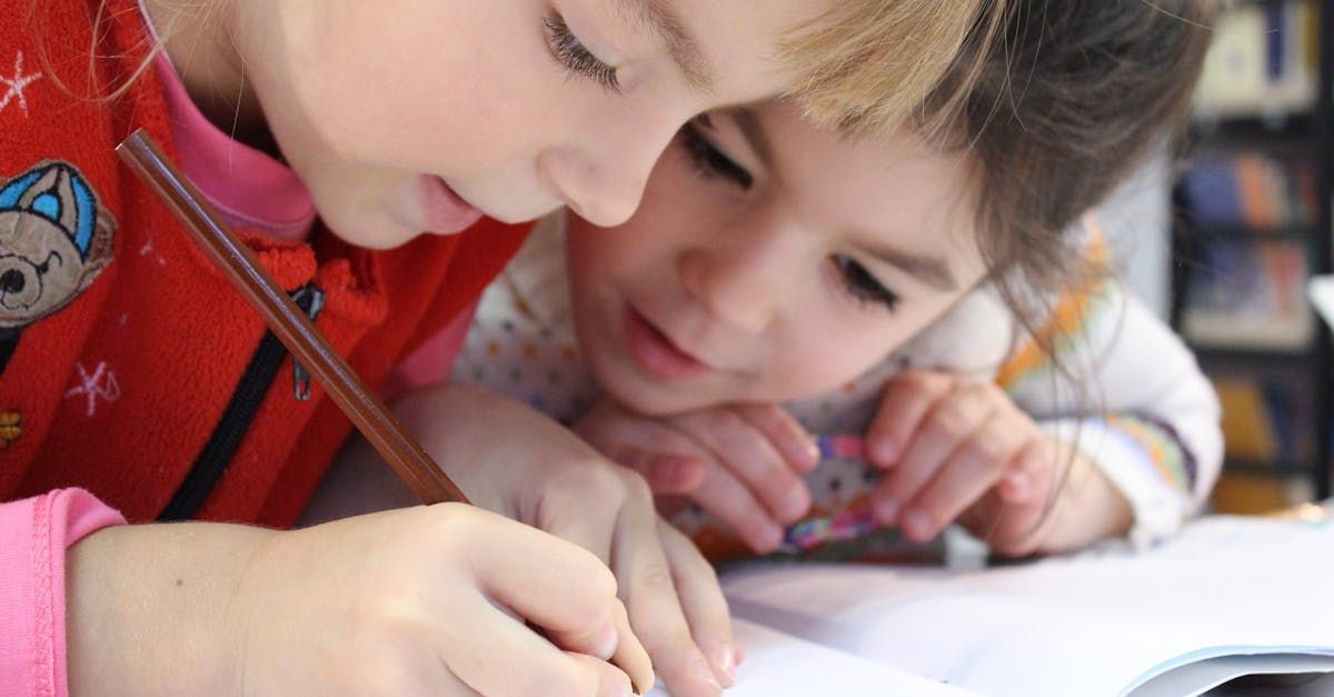 Two young girls are sitting at a table writing in a notebook.