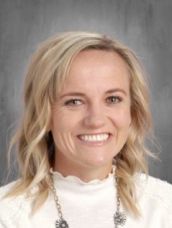 A woman wearing a white shirt and a necklace is smiling for the camera.