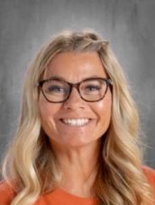A woman wearing glasses and an orange shirt is smiling for the camera.