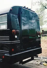 a black school bus is parked on the side of the road .