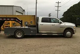 a silver truck with a flatbed trailer attached to it is parked in a gravel lot .