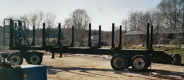 a large log trailer is parked in a dirt lot .