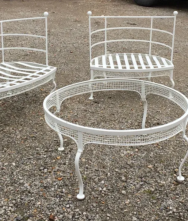 a white wrought iron bench , chair , and table are sitting on a gravel road .