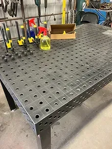 a welding table with holes in it is sitting on the floor in a garage .