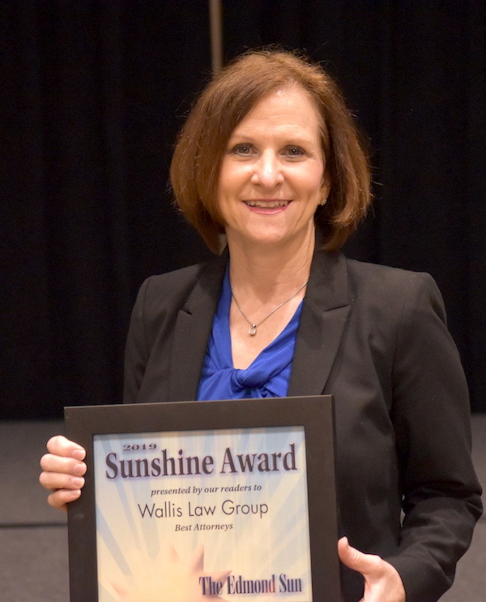 A woman in a suit is holding a sunshine award