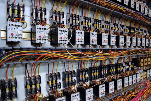Electrical control panel with rows of circuit breakers, contactors, and multicolored wiring on a wall-mounted rack.