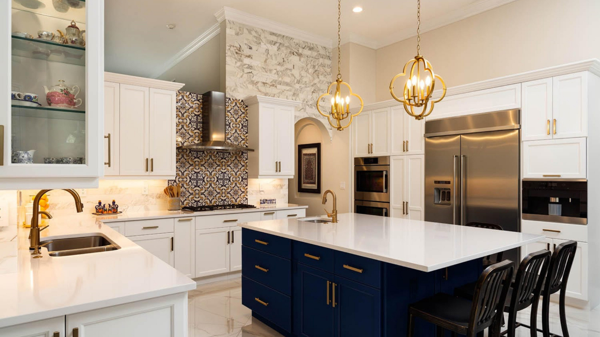 A luxury kitchen with white cabinets, a large navy blue island with seating, patterned tile backsplash, and gold accents.