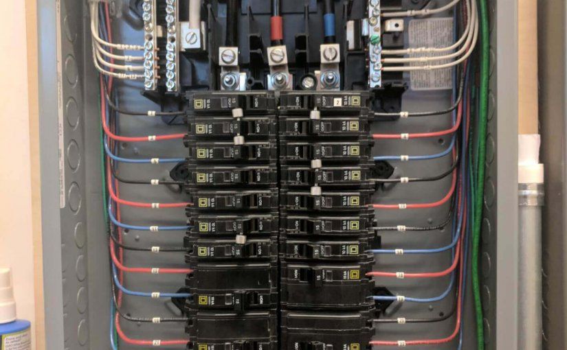 Open electrical panel with neatly arranged circuit breakers and color-coded wiring connected to ground and neutral bars.