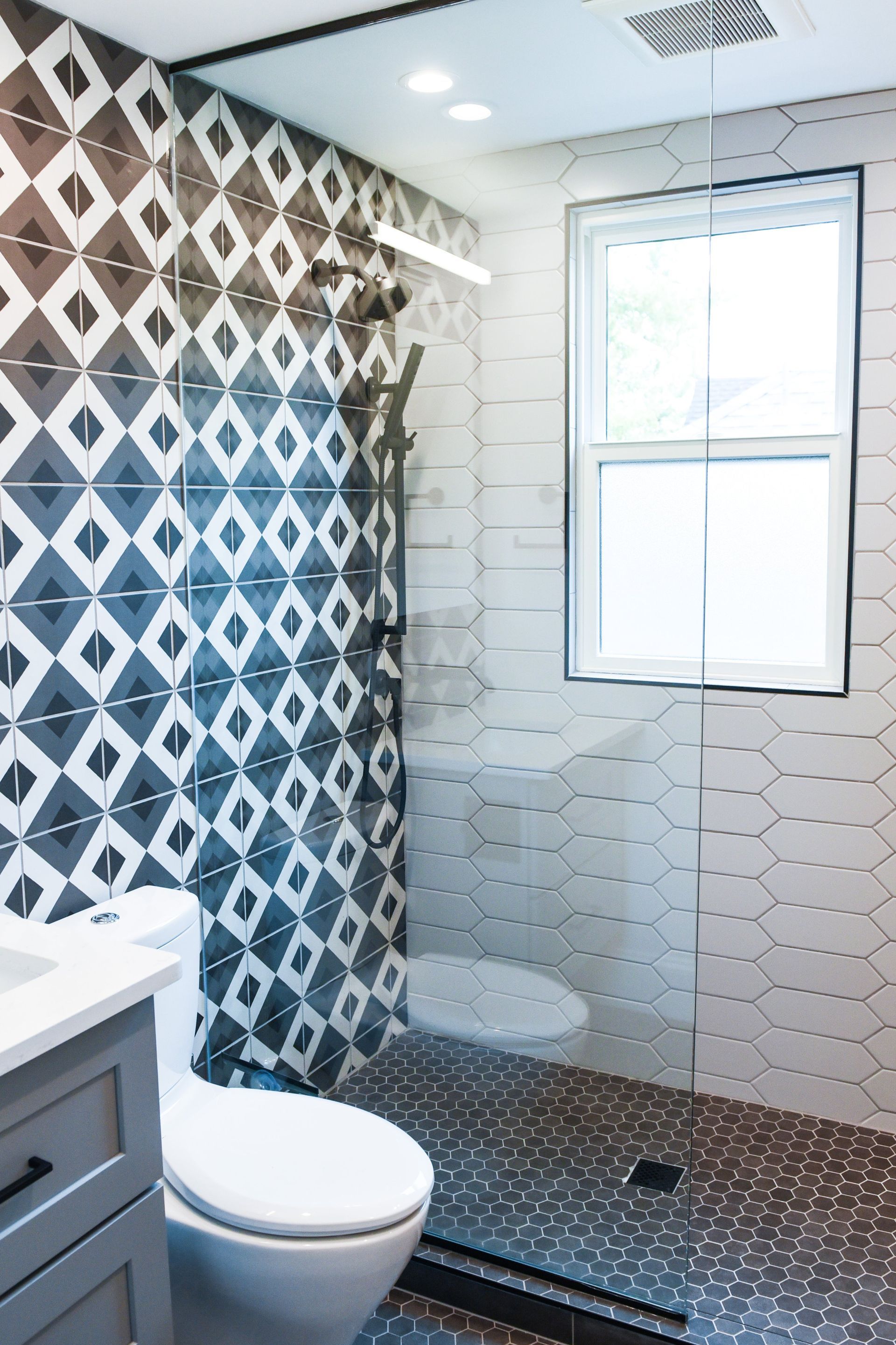 A modern bathroom featuring a walk-in shower with patterned tiles, white hexagonal wall tiles, and a white toilet.