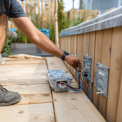 A person connects electrical wiring to a junction box mounted on a wooden deck structure.