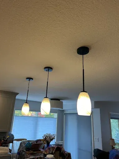 Three pendant lights with frosted glass shades and dark fixtures hang from a textured ceiling in a kitchen area.