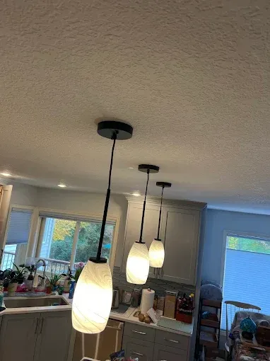 Three modern pendant lights with textured white glass shades and black hardware hanging in a kitchen.