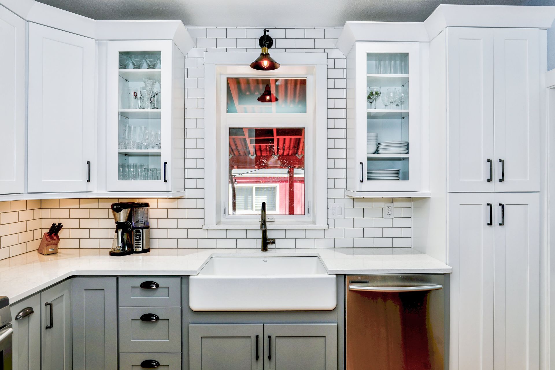 A bright kitchen with white subway tile backsplash, white upper cabinets, and gray lower cabinets surrounding a sink.
