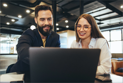 A man and a woman are looking at a laptop computer.