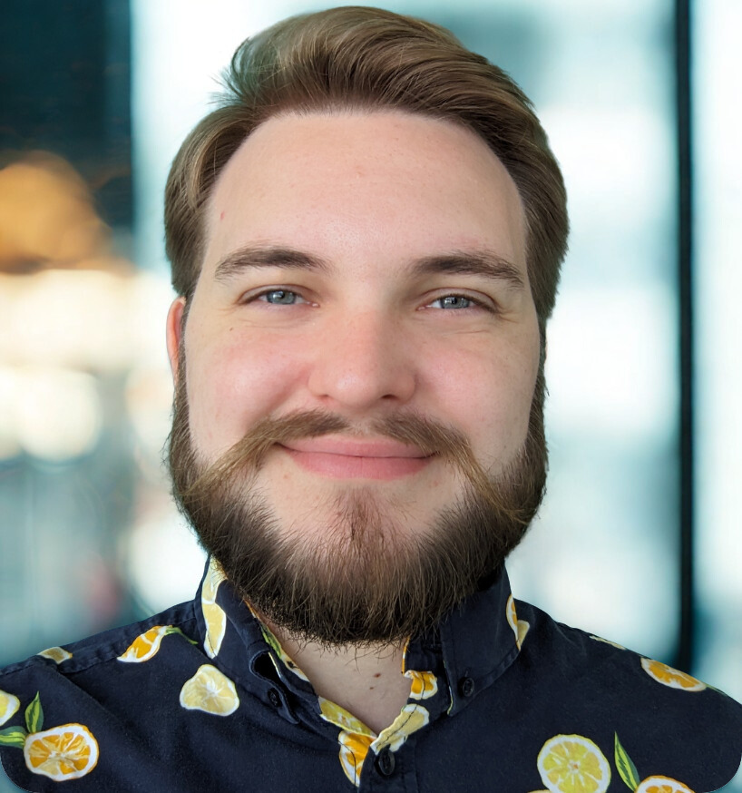 Man with a beard and a lemon-print shirt smiles in front of a teal wall.