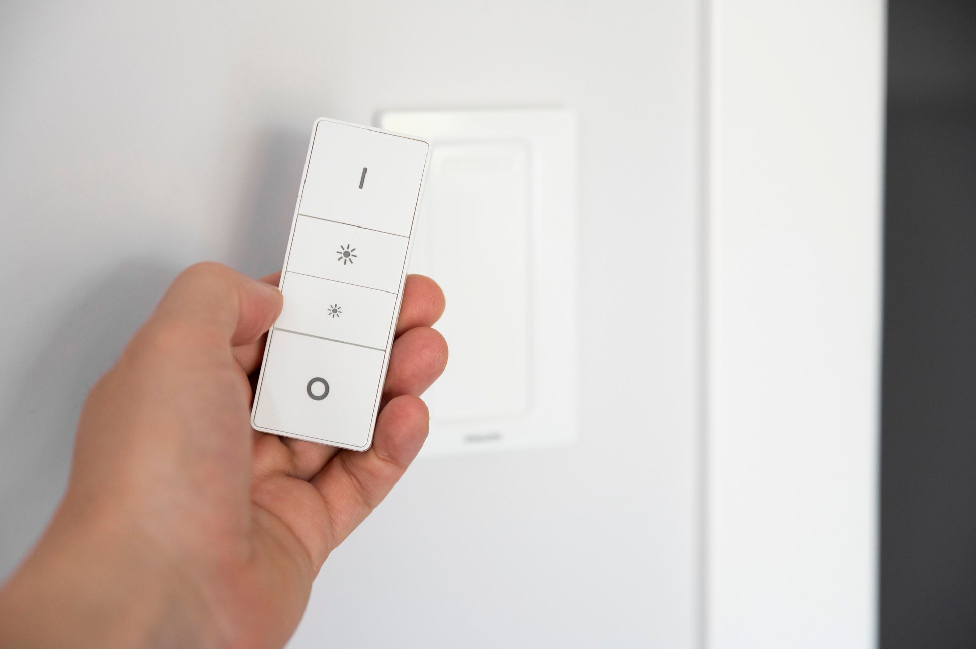 A person is holding a remote control in front of a light switch.