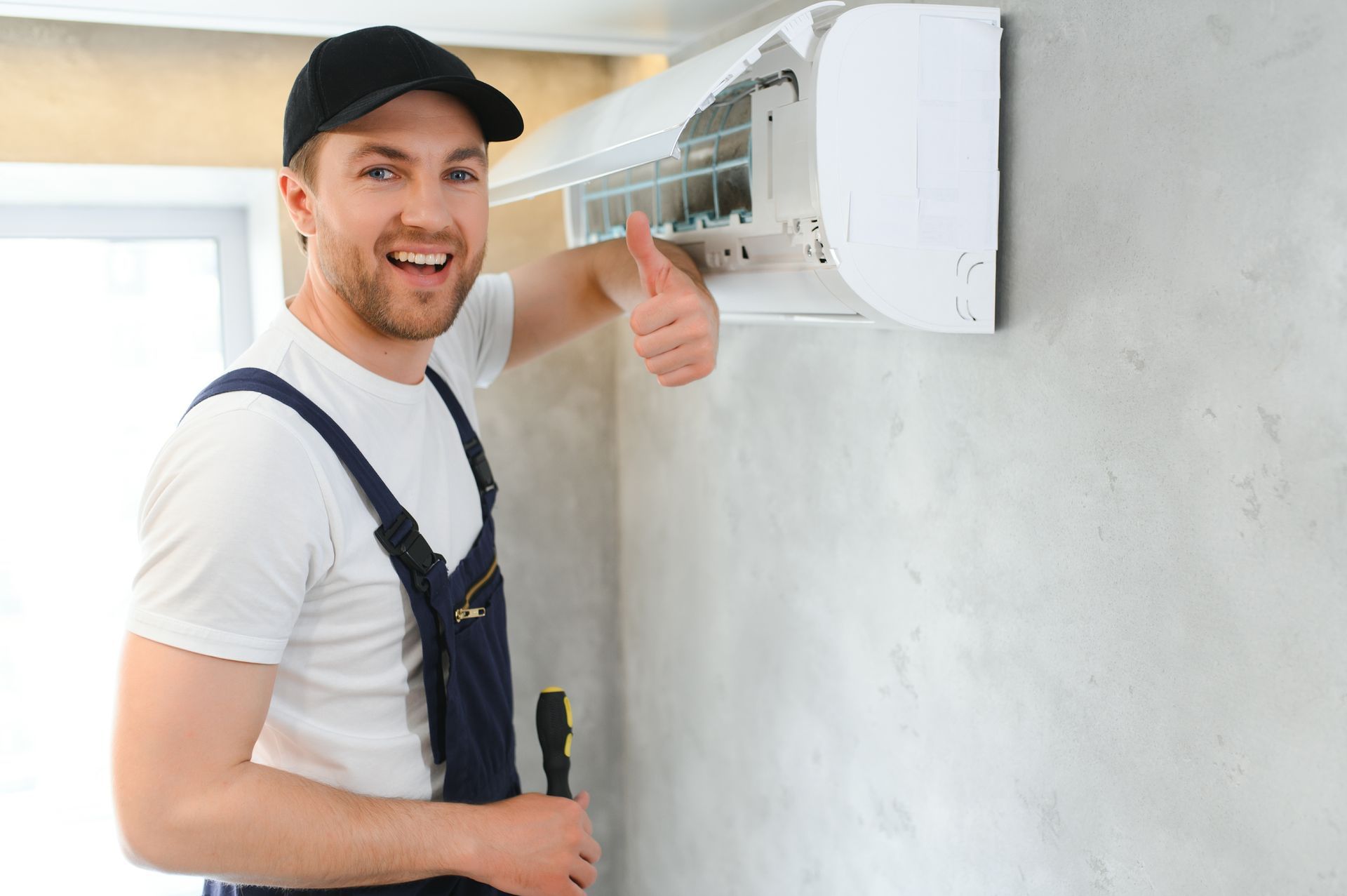 A man is fixing an air conditioner and giving a thumbs up.