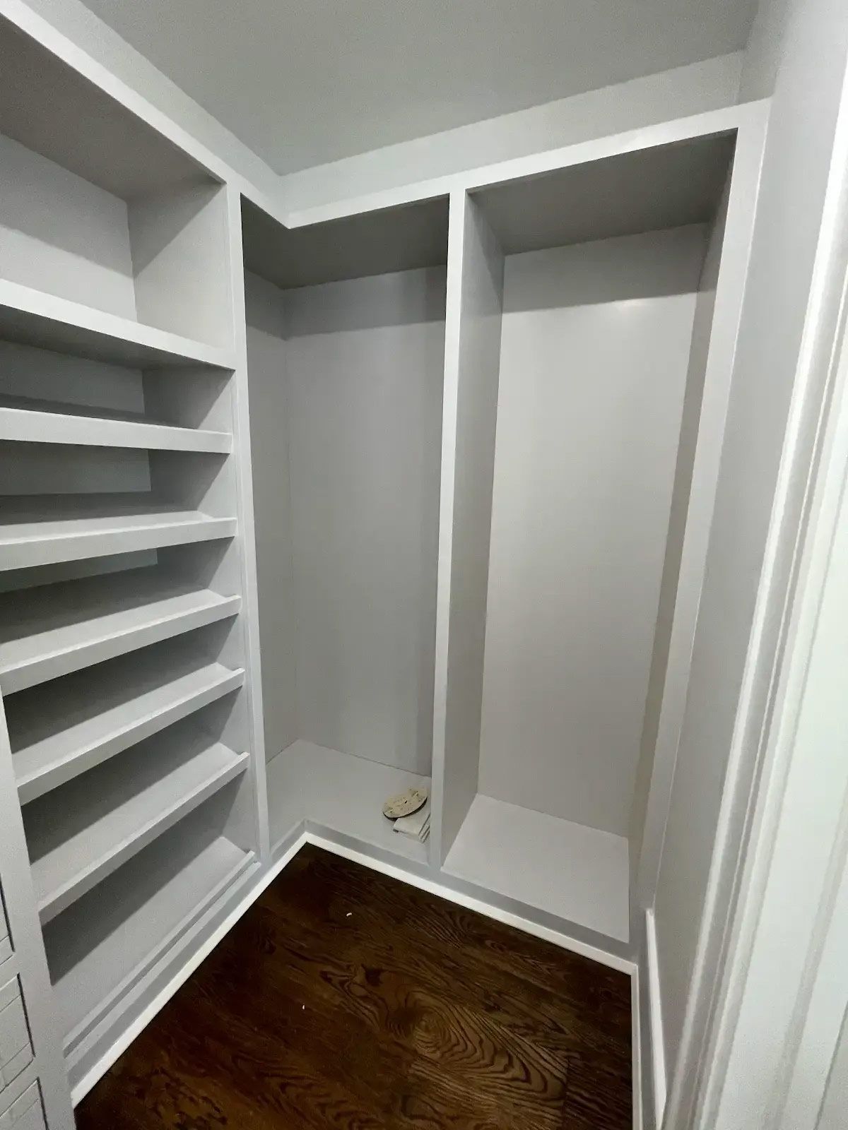 A walk in closet with lots of shelves and a wooden floor