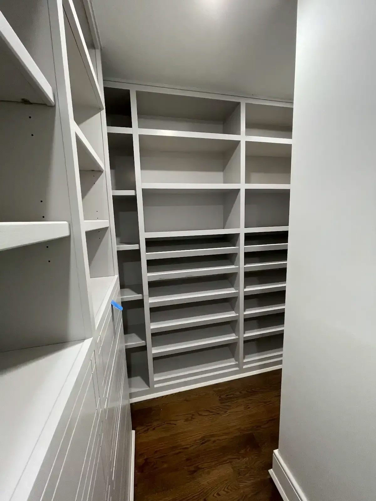 A walk in closet with lots of shelves and a wooden floor