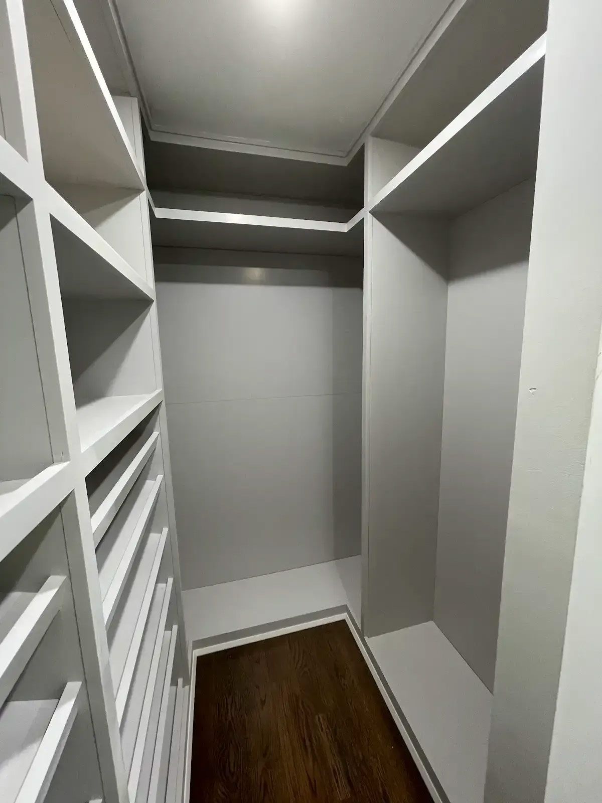 A walk in closet with lots of shelves and a wooden floor
