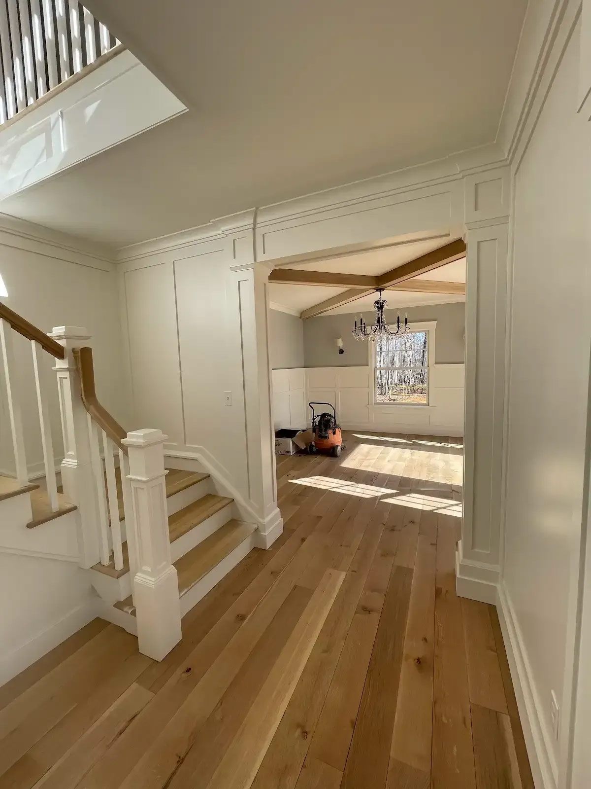 A hallway with wooden floors and stairs leading to a living room