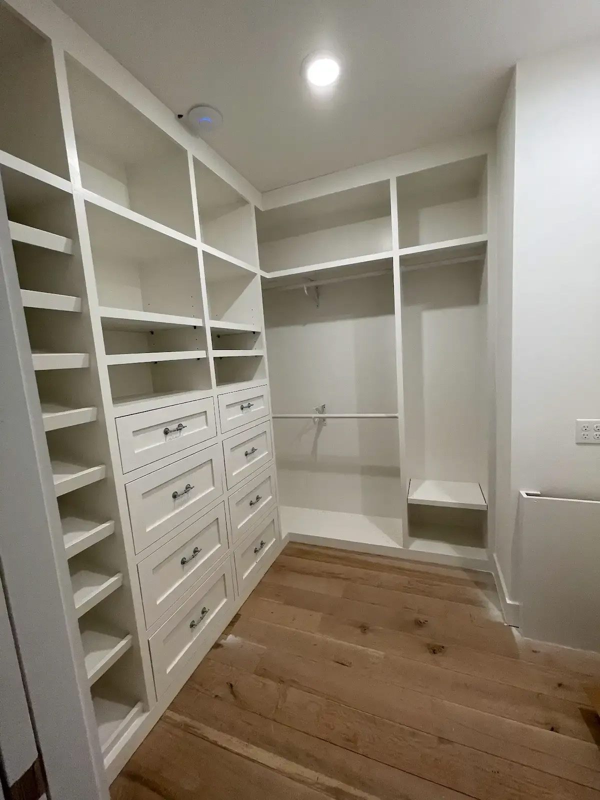 A walk in closet with lots of shelves and drawers and a wooden floor