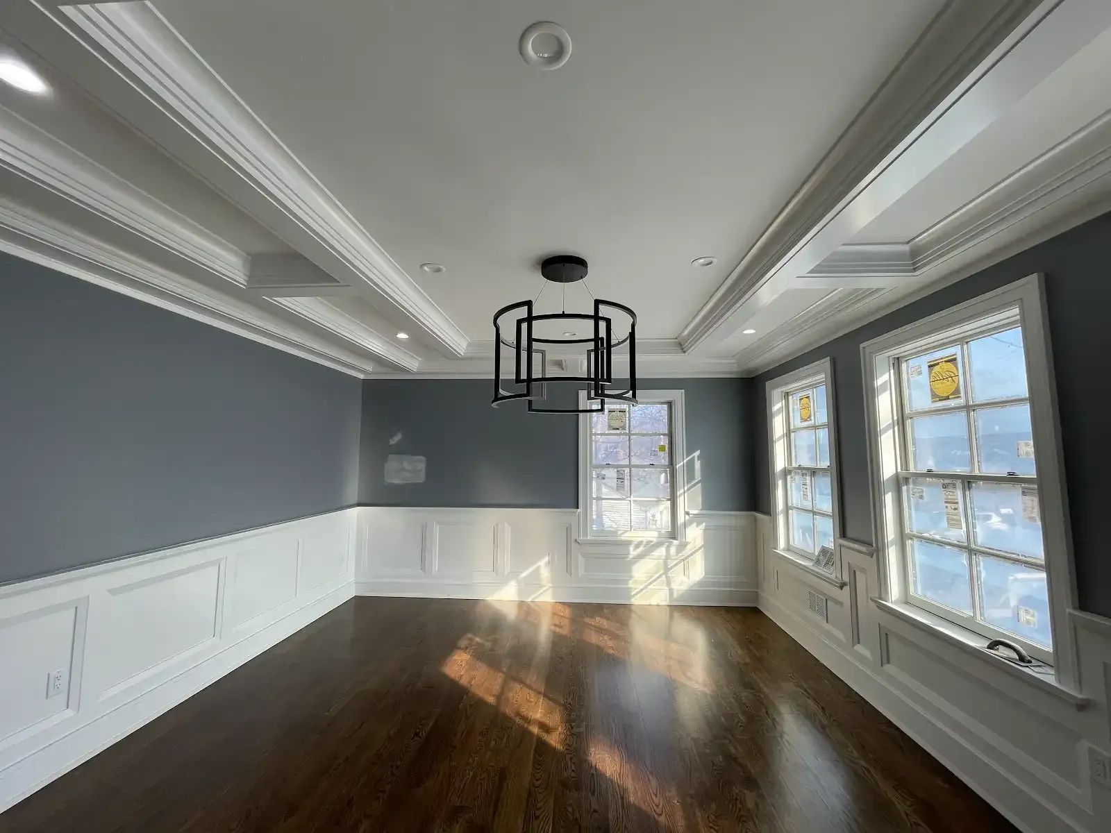 A large empty room with hardwood floors and a chandelier hanging from the ceiling