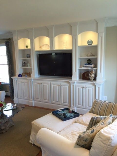 A living room with a couch, ottoman, shelves and a flat screen tv