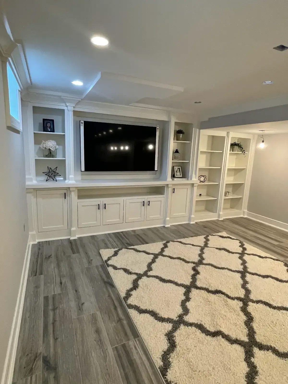 A living room with a couch, ottoman, shelves and a flat screen tv