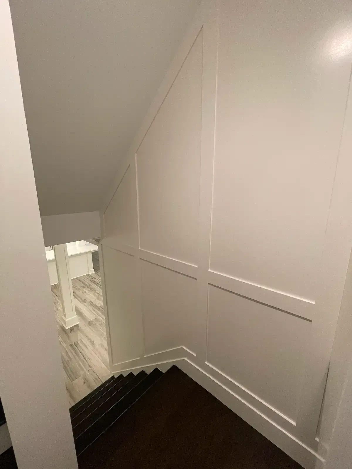 A staircase with a white wall and black steps leading up to the second floor