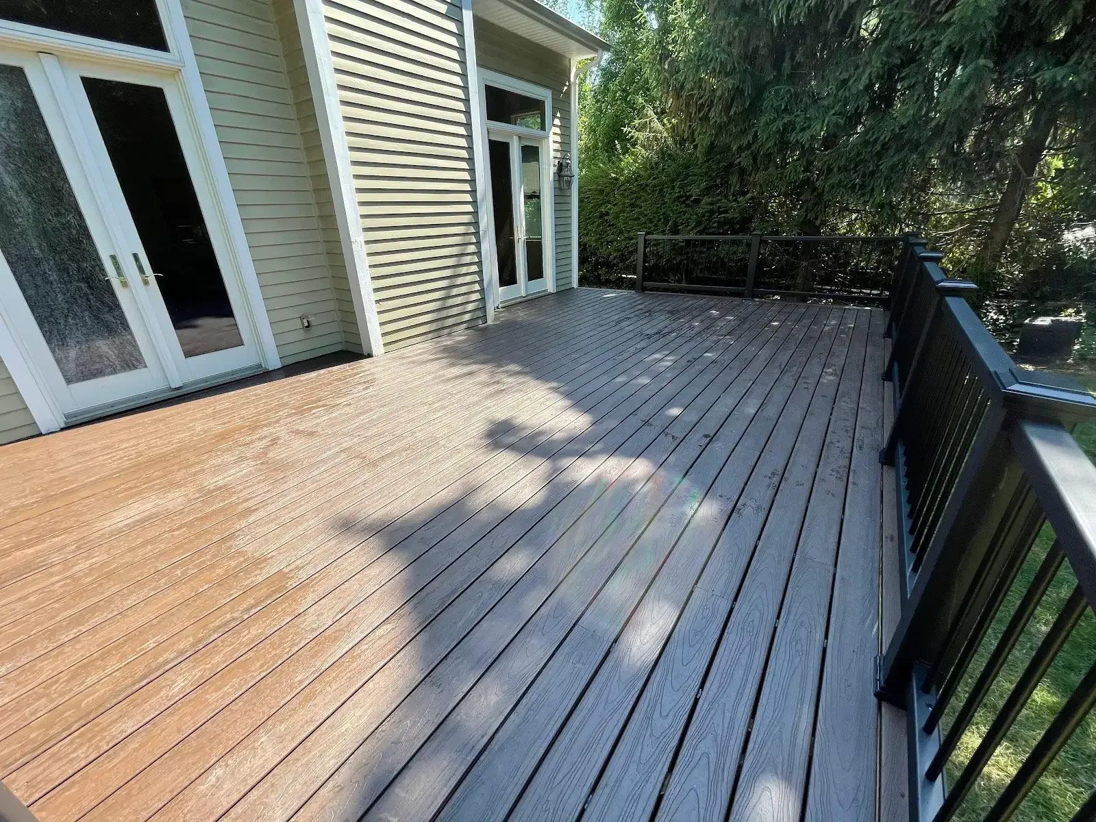 A wooden deck with a black railing in front of a house
