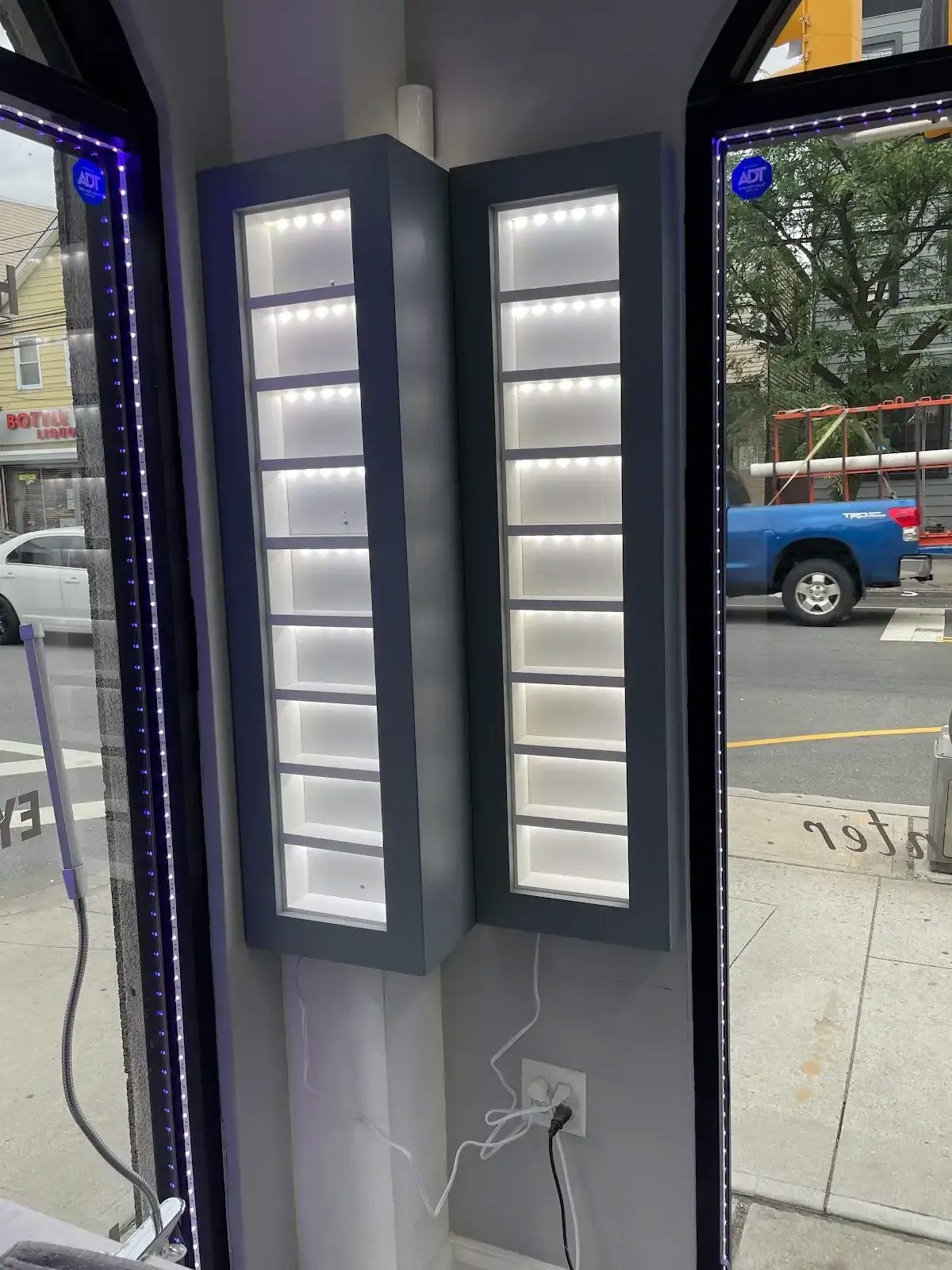 A blue truck is parked on the side of the road in front of a store window